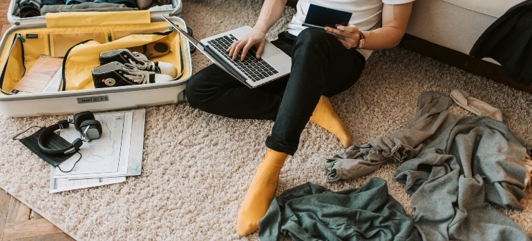 Person packing clothing and electronics in a suitcase, showcasing an orderly approach to moving prep.